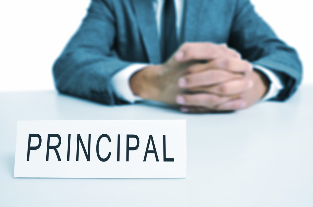 shutterstock a man wearing a suit sitting in a desk with a signboard in front of him with the word principal written in it