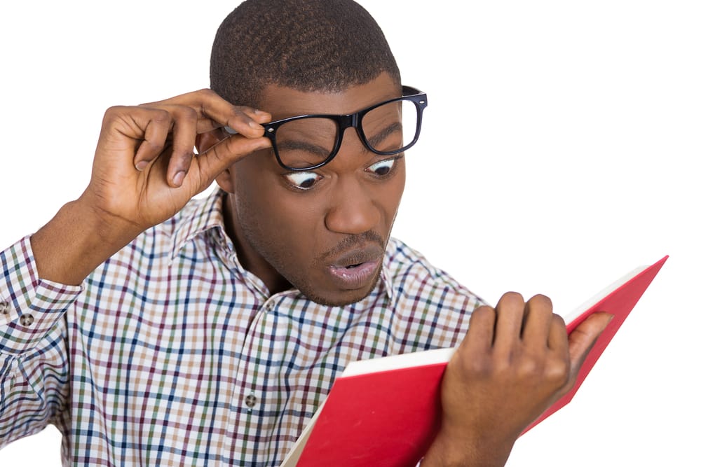 shutterstock_168534788 Closeup portrait of young man, with wide opened eyes staring at a book page, shocked, surprised by the twists and turn of story, isolated on white background. Human emotion, facial expression, feeling